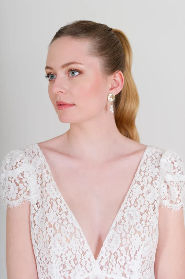 Mariée naturelle. Cheveux tiré et plaqués avec queue de cheveux élégante. Boucles d'oreilles plaqué or et perles d'eau douce bohèmes. Robe de mariée en dentelle