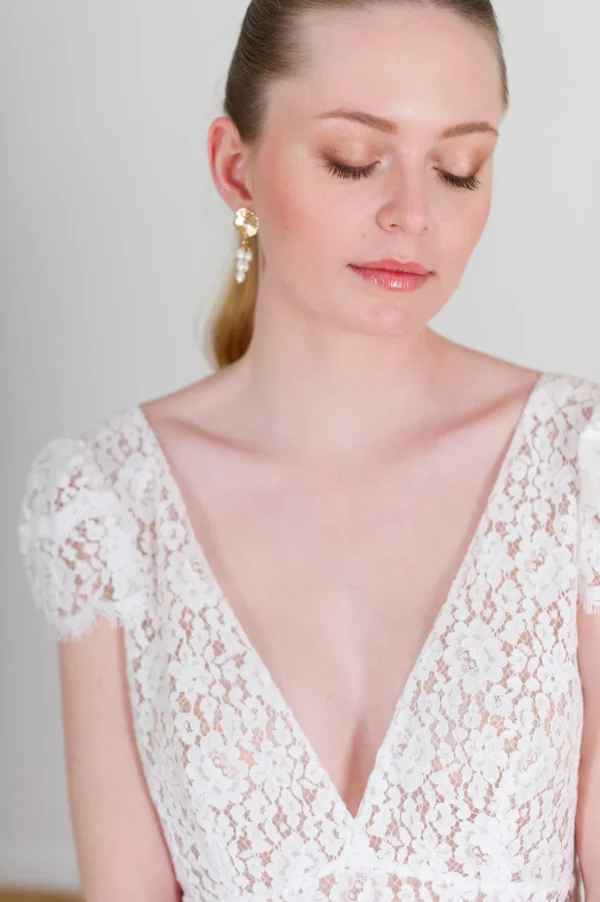 Mariée naturelle. Cheveux tiré et plaqués avec queue de cheveux élégante. Boucles d'oreilles plaqué or et perles d'eau douce bohèmes. Robe de mariée en dentelle