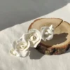 Barette originale ornée de roses blanches de porcelaine froide. L'accessoire coiffure mariée est posé sur un morceau de bois.