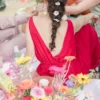 Coiffure bohème avec les épingles Isabella. Longue tresse. Robe rouge dos nu sur un tapis de fleurs colorées.
