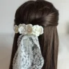 demi queue sur cheveux bruns attachée avec une barette de fleurs blanches de porcelaine froide. L'accessoire surmonte le voile de la mariée