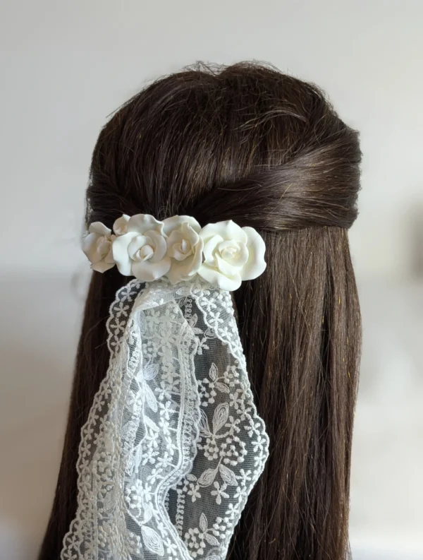 demi queue sur cheveux bruns attachée avec une barette de fleurs blanches de porcelaine froide. L'accessoire surmonte le voile de la mariée