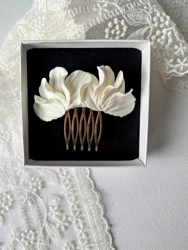 Peigne MARIA 6 <p>MARIA, c'est une branche de pétales blancs en porcelaine froide, longue d'environ 8 cm, montée sur un peigne doré. Ce peigne pétales blancs porcelaine se pose aussi bien sur le côté d'un chignon que sur une demi-coiffure.</p><ul><li>Fait main dans mon atelier du Pays Basque</li><li>Pétales en porcelaine froide, peigne en laiton doré</li><li>Ornement d'environ 8 × 3 cm</li></ul> Gros plan sur MARIA dans l'écrin : pétales blancs ondulés au-dessus des dents dorées