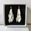 Boucles d'oreilles mariage pendantes. Or et pétales de porcelaine froide. Mariée moderne et élégante