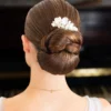 Mariée de dos coiffée d'un chignon bas structuré. Le chignon est orné d'un bijou de cheveux de type peigne de mariage. Le peigne est façonné main en porcelaine froide et perles fines