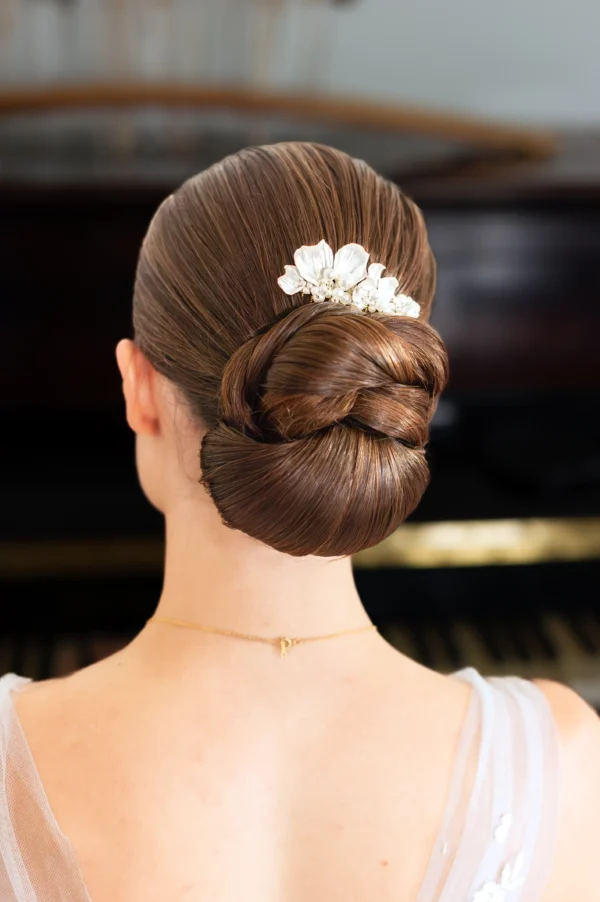 Mariée de dos coiffée d'un chignon bas structuré. Le chignon est orné d'un bijou de cheveux de type peigne de mariage. Le peigne est façonné main en porcelaine froide et perles fines