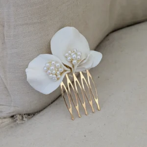 Barrette de mariage minimaliste chic posé sur un fauteuil en lin ancien. La barette à cheveux est ornée de pétales de porcelaine façonnés main et orné dans son coeur d'un groupe de perles de couleur ivoire. Accessoire cheveux perles