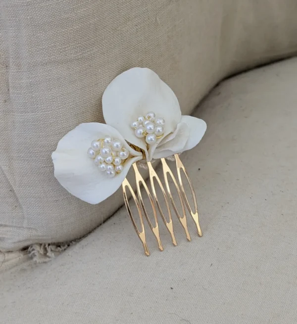Barrette de mariage minimaliste chic posé sur un fauteuil en lin ancien. La barette à cheveux est ornée de pétales de porcelaine façonnés main et orné dans son coeur d'un groupe de perles de couleur ivoire. Accessoire cheveux perles