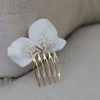 Barrette de mariage minimaliste chic posé sur un fauteuil en lin ancien. La barette à cheveux est ornée de pétales de porcelaine façonnés main et orné dans son coeur d'un groupe de perles de couleur ivoire