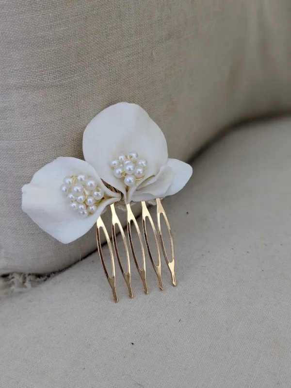 Barrette de mariage minimaliste chic posé sur un fauteuil en lin ancien. La barette à cheveux est ornée de pétales de porcelaine façonnés main et orné dans son coeur d'un groupe de perles de couleur ivoire