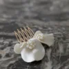 Barrette de mariage minimaliste chic posé à plat. La barette à cheveux est ornée de pétales de porcelaine façonnés main et orné dans son coeur d'un groupe de perles de couleur ivoire
