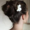 Mariée coiffée d'un chignon haut effet coiffé decoiffé orné d'un peigne chic et minimaliste. Le peigne présente des pétales façonnés main ornés d'un groupe de perles à leur base.