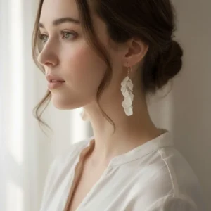 Mariée naturelle et élégante avec boucles d'oreilles pendantes blanches ornées de petites feuilles de porcelaine. Coiffure chignon bas