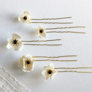 Set d'épingles à chignon pour le mariage posés à plat à côté d'un voile de mariée. Pics à chignon ornés de petites fleurs de porcelaine pésentant dans leur coeur un cristal noir et des étamines dorées