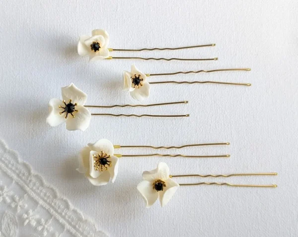 Set d'épingles à chignon pour le mariage posés à plat à côté d'un voile de mariée. Pics à chignon ornés de petites fleurs de porcelaine pésentant dans leur coeur un cristal noir et des étamines dorées
