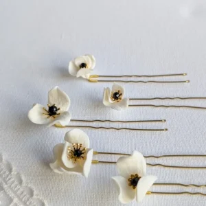 Set d'épingles à chignon pour le mariage posés à plat à côté d'un voile de mariée. Pics à chignon ornés de petites fleurs de porcelaine pésentant dans leur coeur un cristal noir et des étamines dorées