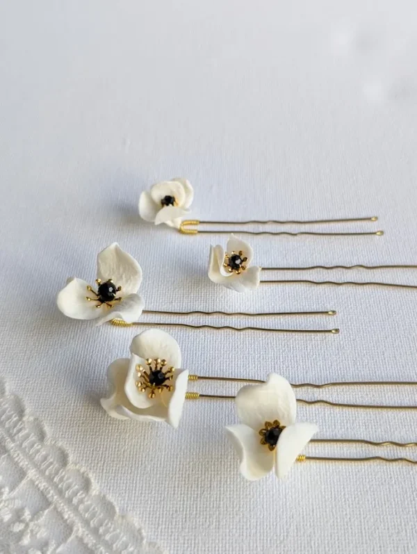 Set d'épingles à chignon pour le mariage posés à plat à côté d'un voile de mariée. Pics à chignon ornés de petites fleurs de porcelaine pésentant dans leur coeur un cristal noir et des étamines dorées