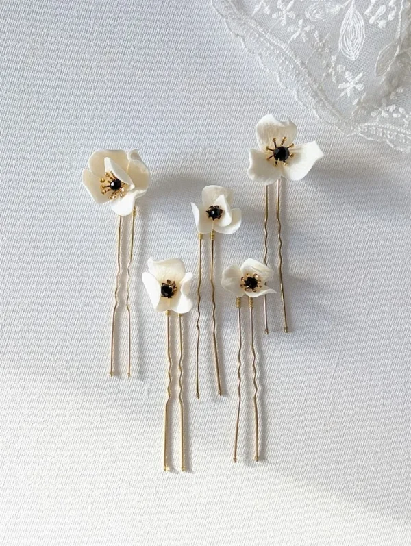Set d'épingles à chignon pour le mariage posés à plat à côté d'un voile de mariée. Pics à chignon ornés de petites fleurs de porcelaine pésentant dans leur coeur un cristal noir et des étamines dorées