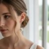 Gros plan sur APOLLINE portée avec un chignon bas, près d'une fenêtre