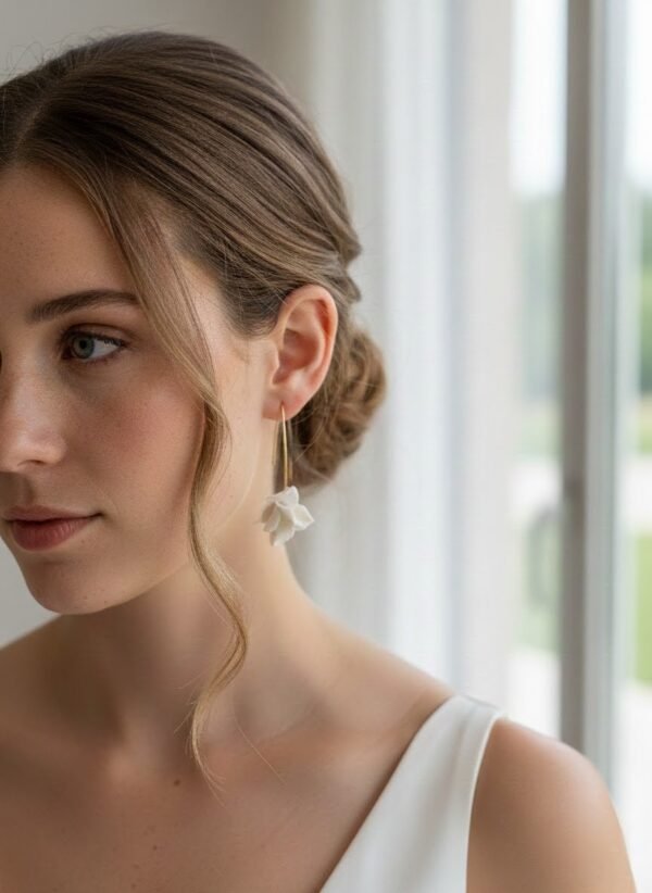 Boucles d'oreilles APOLLINE 4 Apolline, c'est un bouton de fleur en porcelaine froide, posé sur un long crochet fin qui traverse le lobe. Des boucles d'oreilles aériennes, pour les mariées qui aiment le naturel. <ul> <li>Faites main dans mon atelier du Pays Basque</li> <li>Long crochet en acier inoxydable 304, doré à l'or fin 14k ou argenté</li> <li>Fleur de 1,5 cm · longueur d'environ 5 cm · 2 g</li> </ul> Gros plan sur APOLLINE portée avec un chignon bas, près d'une fenêtre