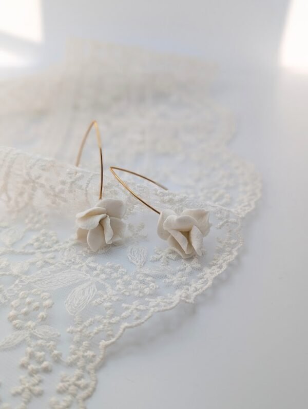Boucles d'oreilles APOLLINE 3 Apolline, c'est un bouton de fleur en porcelaine froide, posé sur un long crochet fin qui traverse le lobe. Des boucles d'oreilles aériennes, pour les mariées qui aiment le naturel. <ul> <li>Faites main dans mon atelier du Pays Basque</li> <li>Long crochet en acier inoxydable 304, doré à l'or fin 14k ou argenté</li> <li>Fleur de 1,5 cm · longueur d'environ 5 cm · 2 g</li> </ul> APOLLINE posées sur une dentelle : boutons de fleur en porcelaine froide mate et longs crochets dorés