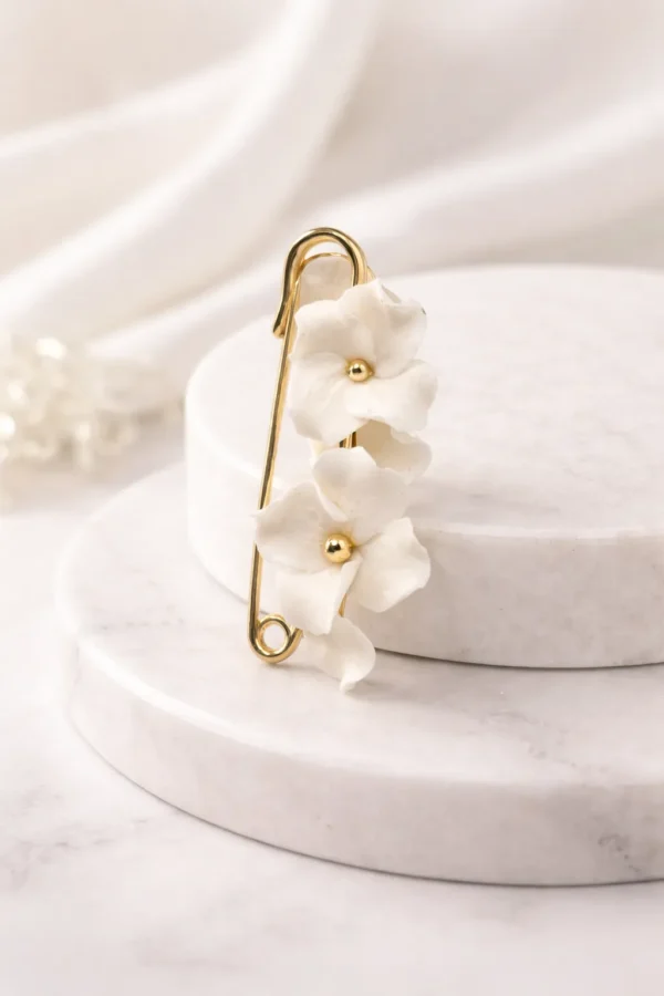 Attache-traîne DIANE 1 <p>Une épingle dorée et quelques fleurs blanches en porcelaine froide : DIANE est une attache-traîne mariée qui relève la traîne après la cérémonie, pour danser librement. Elle sert ensuite de broche ou d'attache de boléro.</p><ul><li>Fait main au Pays basque, en France</li><li>Fleurs en porcelaine froide, épingle en laiton</li><li>Longueur : 5 cm</li></ul> Attache-traîne mariée DIANE : fleurs blanches en porcelaine froide sur une épingle dorée, by Marguerite