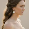 Mariée aux cheveux longs ondulés en demi-queue portant les boucles d'oreilles VIVIENNE