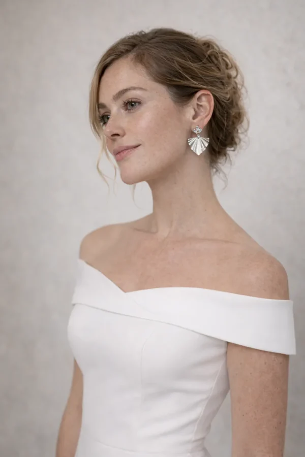 Mariée en robe à épaules dénudées et chignon bas portant les boucles d'oreilles VICTORIA argentées