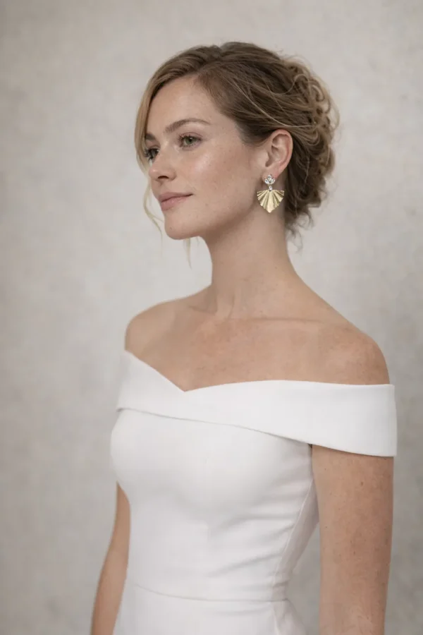 Mariée en robe à épaules dénudées et chignon bas portant les boucles d'oreilles VICTORIA dorées