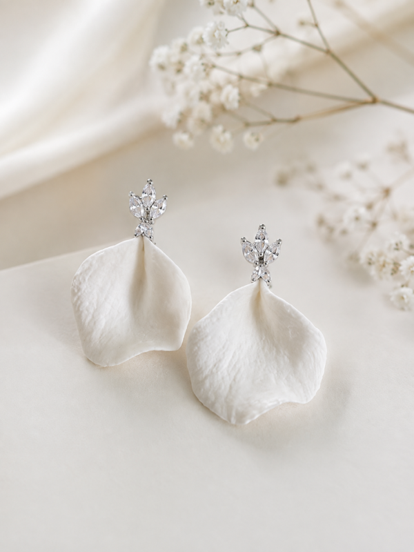 Boucles d'oreilles NOÉMIE 15 Noémie associe la douceur mate de la porcelaine à une étincelle de lumière. Un pétale de porcelaine froide pend sous une petite puce fleur sertie de cristaux, pour des boucles d'oreilles discrètes. <ul> <li>Faites main dans mon atelier du Pays Basque</li> <li>Puce plaquée or 18k ou en laiton argenté, zircone cubique, pétale en porcelaine froide</li> <li>Pétale de 2,5 × 2,3 cm · puce de 1 × 0,8 cm</li> </ul> Boucles d'oreilles mariage argenté, cristaux et pétale de porcelaine froide faites main en France