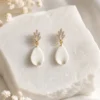 Boucles d’oreilles Kate en porcelaine froide posées sur une pierre blanche texturée, avec détails dorés et cristaux, dans une ambiance lumineuse et épurée.