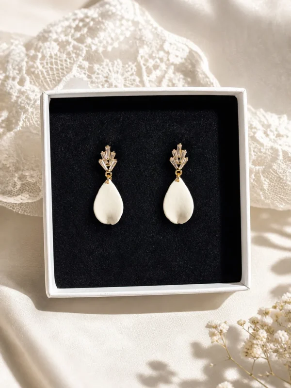 Boucles d'oreilles KATE 1 <p>Kate est une goutte de porcelaine froide, lisse et légèrement recourbée, sous une puce sertie de zirconium. Ces boucles d'oreilles ont une tige adaptée aux oreilles sensibles.</p><ul><li>Faites main dans mon atelier du Pays Basque</li><li>Puce plaquée or 16k sertie de zirconium, tige en acier chirurgical 316</li><li>Longueur totale : environ 4 cm · 1,7 g</li></ul> Boucles d’oreilles mariage Kate présentées dans un écrin blanc, avec goutte en porcelaine froide et puce dorée ornée de cristaux, sur fond textile délicat.