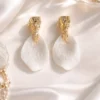 ROXANNE posées sur un satin blanc au soleil : pétales de porcelaine froide en mouvement et puces dorées