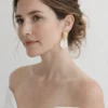 Mariée minimaliste chic aux épaules dénudées portant les boucles d'oreilles ROXANNE en porcelaine et or