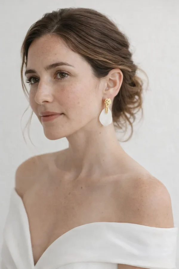 Mariée minimaliste chic aux épaules dénudées portant les boucles d'oreilles ROXANNE en porcelaine et or