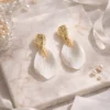 Boucles d'oreilles mariage ROXANNE : pétales blancs en porcelaine froide sous une puce dorée martelée, sur un marbre clair, by Marguerite