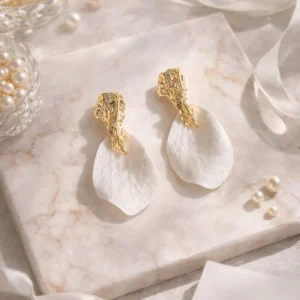 Boucles d'oreilles mariage ROXANNE : pétales blancs en porcelaine froide sous une puce dorée martelée, sur un marbre clair, by Marguerite