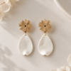 Boucles d’oreilles Zélie dorées avec puce en forme de soleil et pétale blanc en porcelaine froide, création artisanale pour mariage.