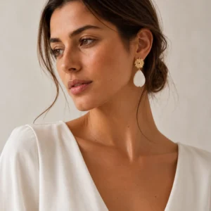 Boucles d’oreilles mariage Zélie dorées et blanches portées par une femme, avec puce soleil et pétale en porcelaine froide.