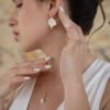 Mariée élégante avec boucles d'oreilles pétales de porcelaine et cristaux.