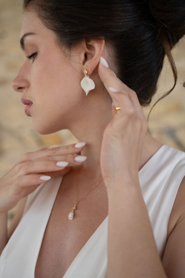 Boucles d'oreilles NOÉMIE 13 Noémie associe la douceur mate de la porcelaine à une étincelle de lumière. Un pétale de porcelaine froide pend sous une petite puce fleur sertie de cristaux, pour des boucles d'oreilles discrètes. <ul> <li>Faites main dans mon atelier du Pays Basque</li> <li>Puce plaquée or 18k ou en laiton argenté, zircone cubique, pétale en porcelaine froide</li> <li>Pétale de 2,5 × 2,3 cm · puce de 1 × 0,8 cm</li> </ul> Mariée élégante avec boucles d'oreilles pétales de porcelaine et cristaux.