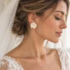 Mariée au chignon bas et voile de tulle portant les puces d'oreilles ALMA, fleur blanche en porcelaine froide sur le lobe