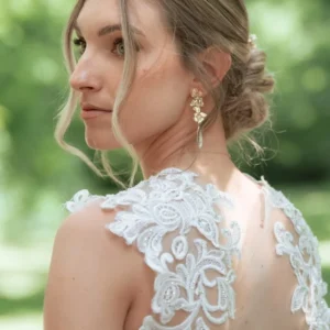 Mariée de profil, chignon bas, portant les boucles d'oreilles NORA avec une robe en dentelle au dos ajouré