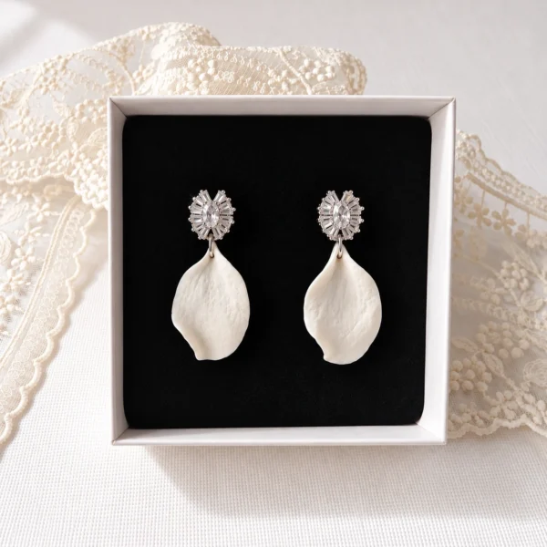 Boucles d'oreilles STELLA 15 Un pétale de porcelaine froide façonné à la main, à l'aspect de pétale de rose, sous une puce sertie de zircones cubiques : STELLA, ce sont des boucles d'oreilles de mariée à pétale de porcelaine, lumineuses et légères, en version dorée ou argentée. <ul> <li>Faites main au Pays basque, en France</li> <li>Pétale en porcelaine froide, puce plaqué or ou plaqué platine et zircones cubiques</li> <li>Pétale d'environ 3 cm · environ 1,7 g par boucle</li> </ul> Boucles d'oreilles STELLA argentées dans leur écrin : pétale de porcelaine froide blanc sous une puce plaqué platine sertie de zircones, by Marguerite