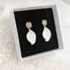 Boucles d'oreilles de mariée STELLA dans leur écrin noir, pétales de porcelaine froide et puces dorées serties de zircones, sur une dentelle, by Marguerite