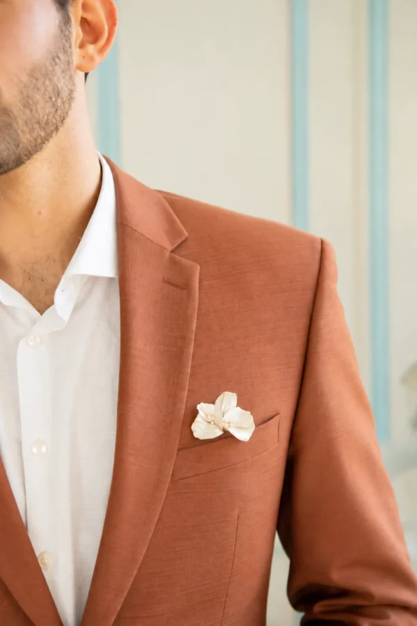 Boutonnière VIVIENNE 2 <p>Trois pétales de porcelaine froide nacrée, striés et légèrement en mouvement, avec de toutes petites perles naturelles en leur cœur : VIVIENNE est une boutonnière nacrée pour le marié. Elle répond à toute la ligne VIVIENNE de la mariée, de la couronne à l’attache-traîne.</p><ul><li>Fait main au Pays basque, en France</li><li>Pétales en porcelaine froide nacrée, petites perles naturelles</li><li>Fleur d’environ 4,8 cm de large et 4 cm de haut · épingle argentée</li></ul> Boutonnière de marié VIVIENNE glissée dans la poche poitrine d’une veste terracotta, chemise blanche, by Marguerite