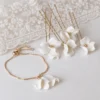 Parure mariée : bracelet DIANE doré à pétales de porcelaine et épingles à cheveux fleurs ADÈLE, posés près d'une dentelle
