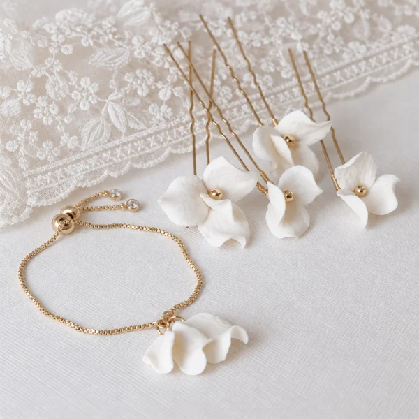 Parure mariée : bracelet DIANE doré à pétales de porcelaine et épingles à cheveux fleurs ADÈLE, posés près d'une dentelle