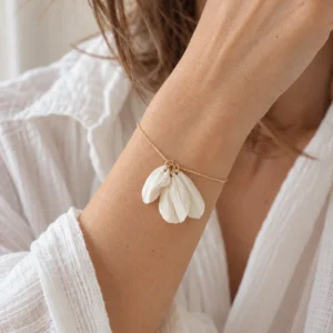Bracelet JUSTINE porté au poignet avec une chemise blanche en gaze de coton, trois pétales blanc mat sur chaîne dorée, by Marguerite