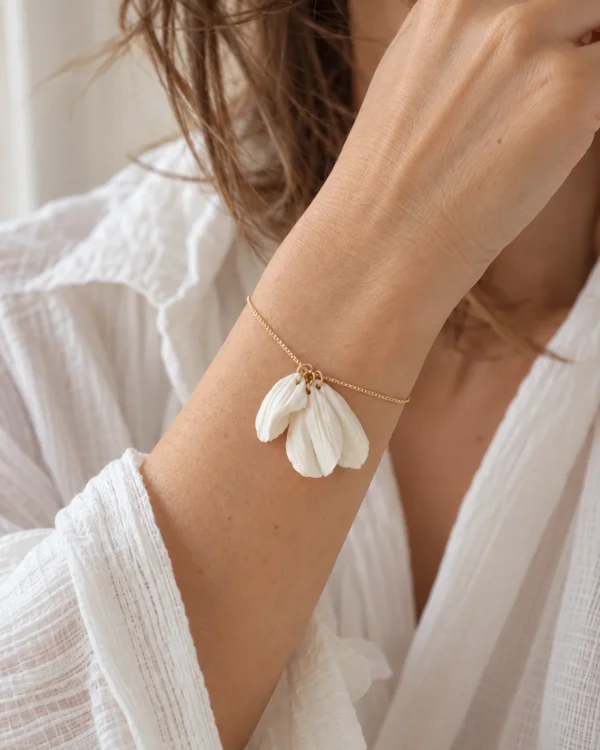 Bracelet JUSTINE porté au poignet avec une chemise blanche en gaze de coton, trois pétales blanc mat sur chaîne dorée, by Marguerite